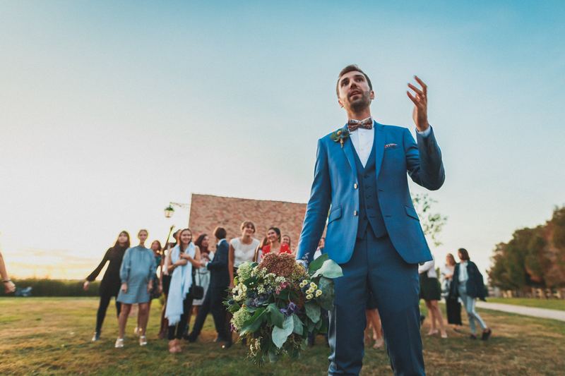 Le marié s’adresse aux invités, bouquet à la main, devant la grange