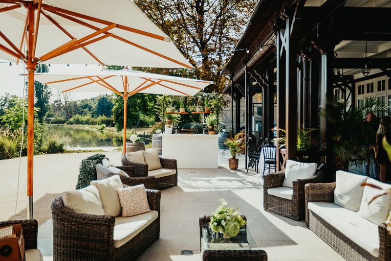 Terrasse aménagée de parasols et de canapés en osier, au bord de l’étang
