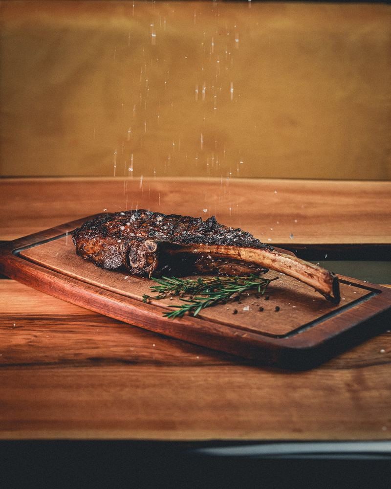Côte de bœuf sur planche de bois, pluie de sel et romarin