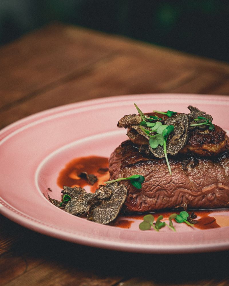 Pièce de bœuf aux truffes noires servie dans une assiette rose