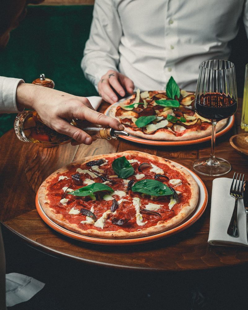 Deux pizzas servies à table, la main du serveur au premier plan