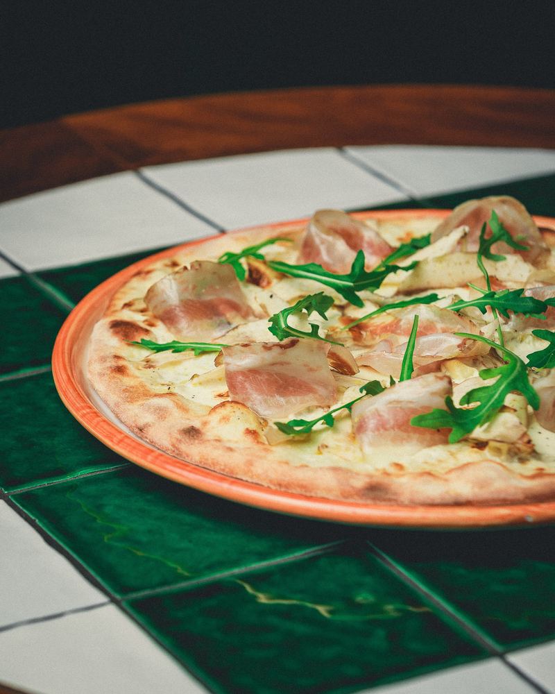 Pizza blanche au jambon cru et roquette sur carrelage vert