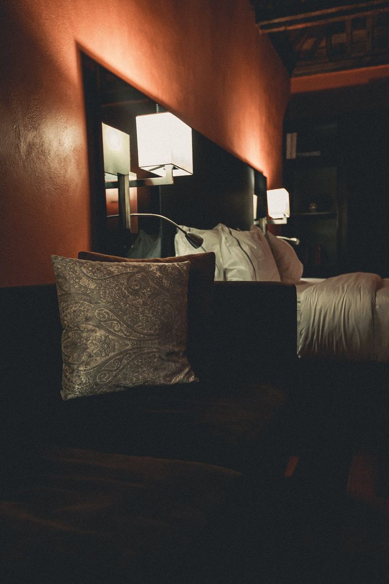 Coin lecture d’une chambre d’hôtel, coussin brodé et liseuse allumée