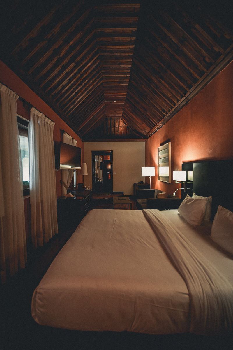 Chambre d’hôtel sous charpente apparente, éclairage chaud