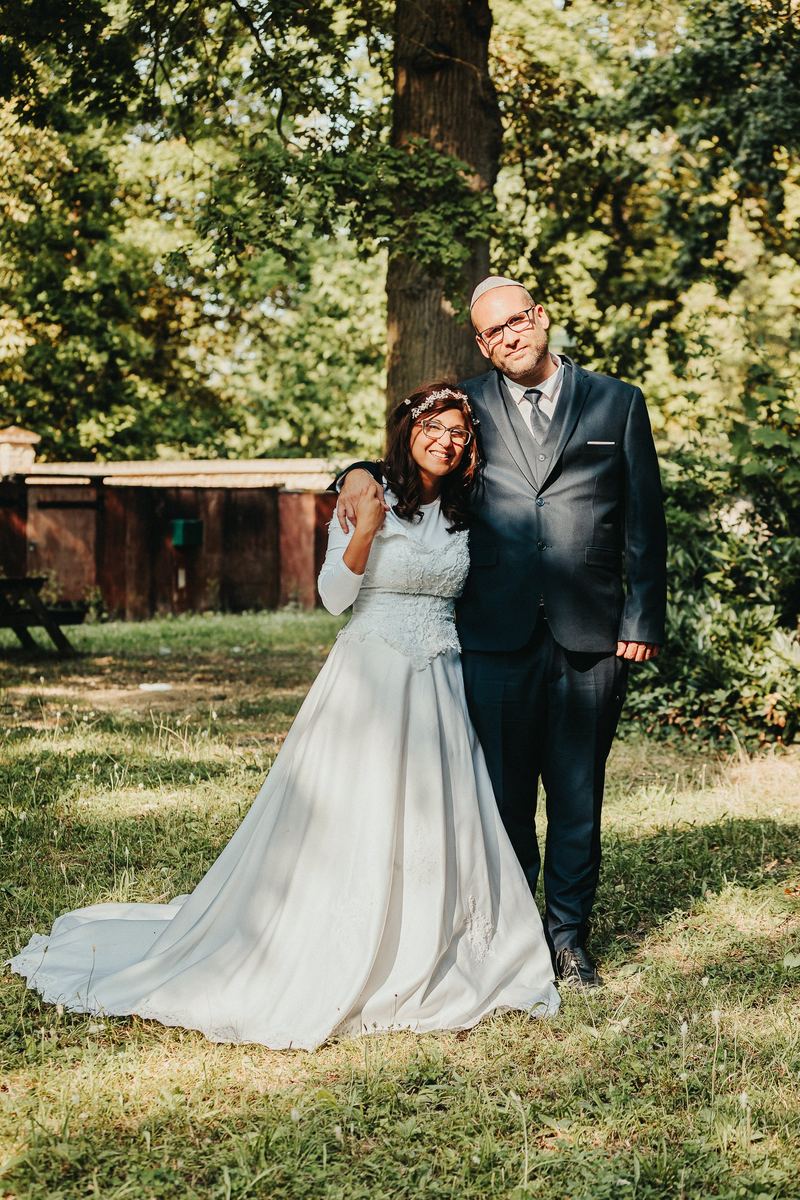 Les mariés posent sous les arbres, robe bleu pâle et costume sombre
