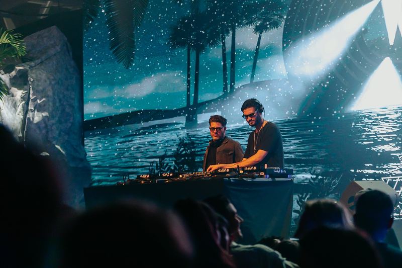 Deux DJ devant un décor de plage projeté sur écran géant