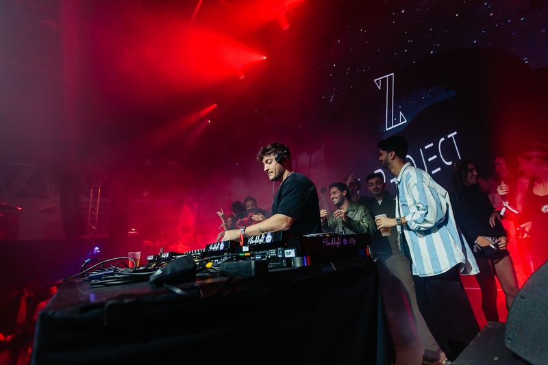 DJ aux platines devant un écran lumineux, salle noyée de rouge