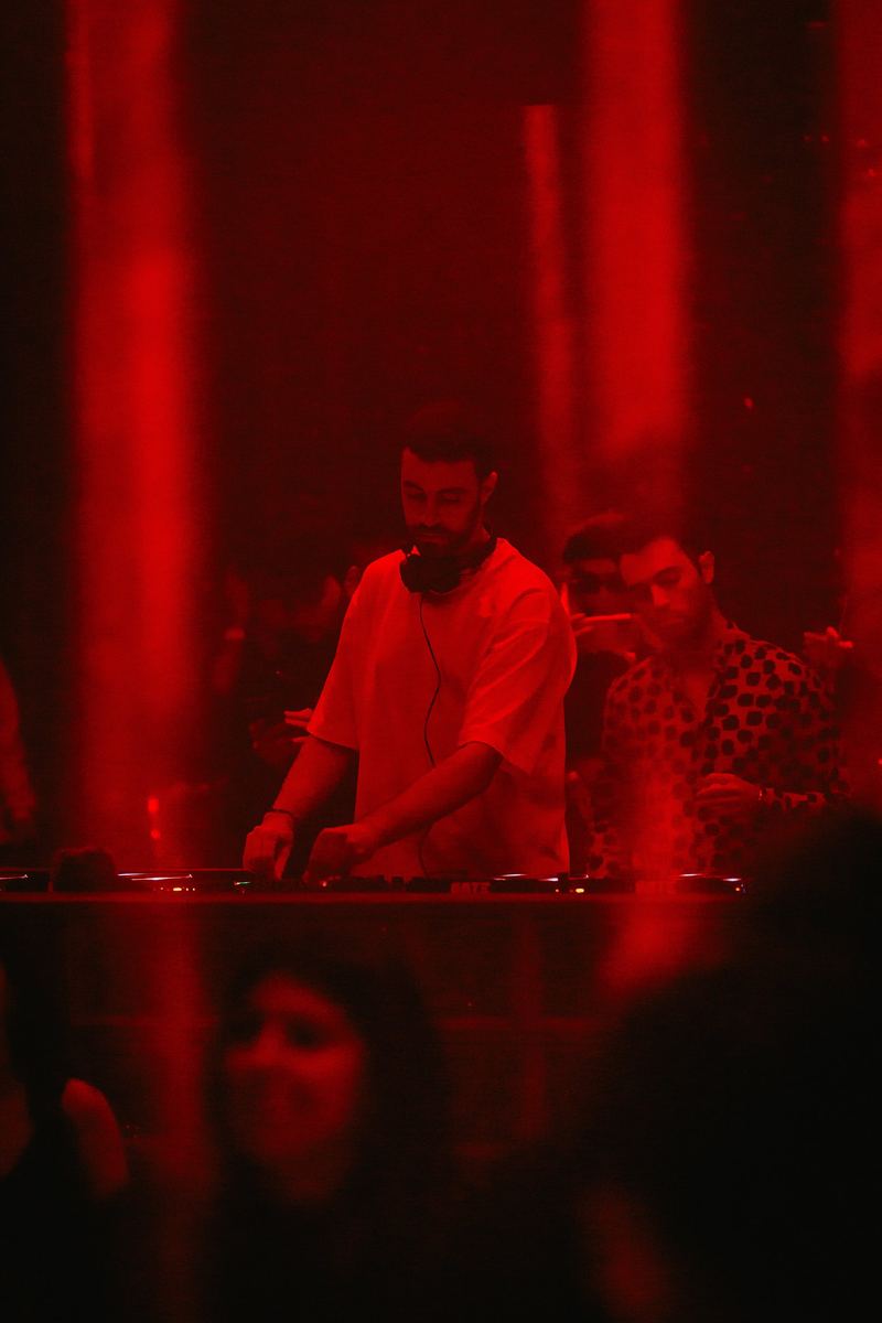 DJ en tenue orange derrière les platines, salle éclairée en rouge
