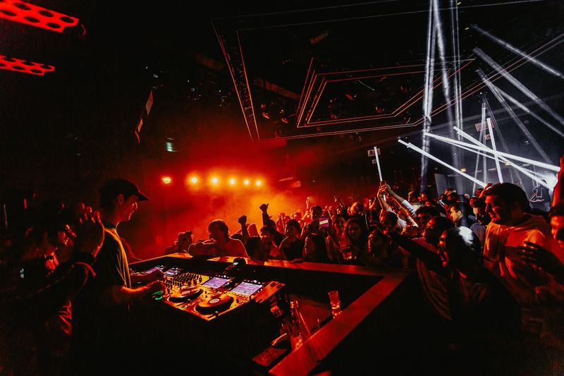 Le public lève les mains devant la cabine du DJ, lasers en fond