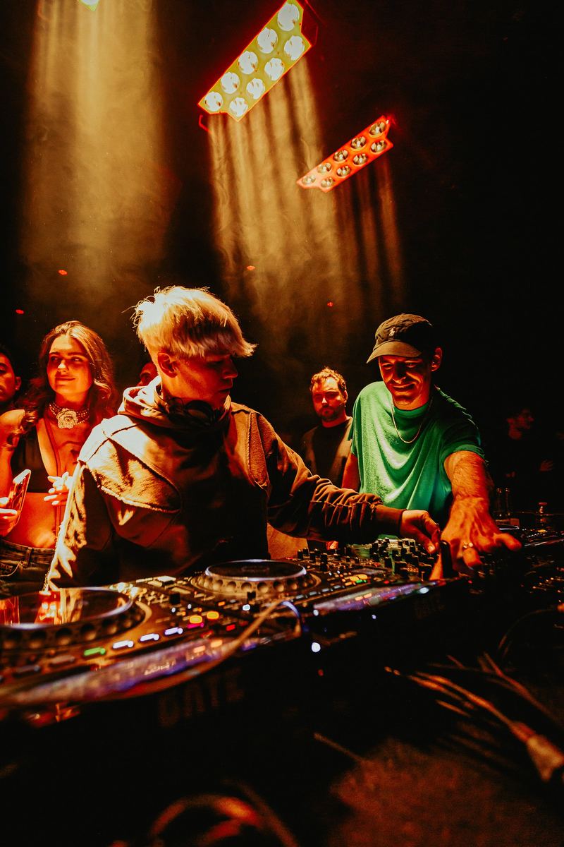 DJ aux platines dans la lumière chaude, public au premier plan
