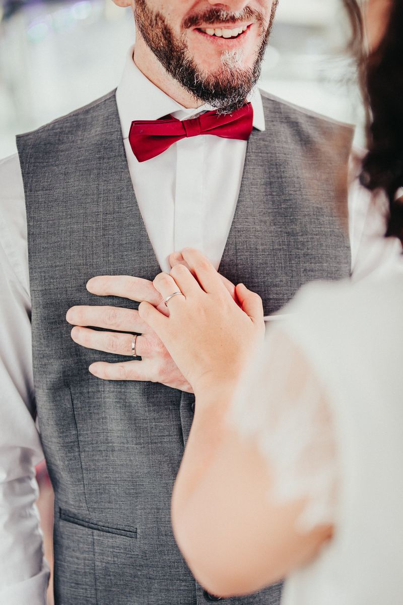 Les mains de la mariée posées sur le gilet du marié, nœud papillon bordeaux