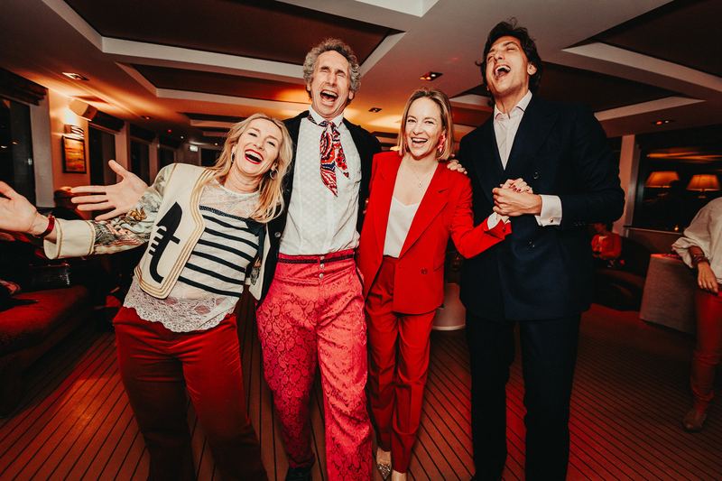 Quatre invités éclatent de rire, bras ouverts, pendant la soirée