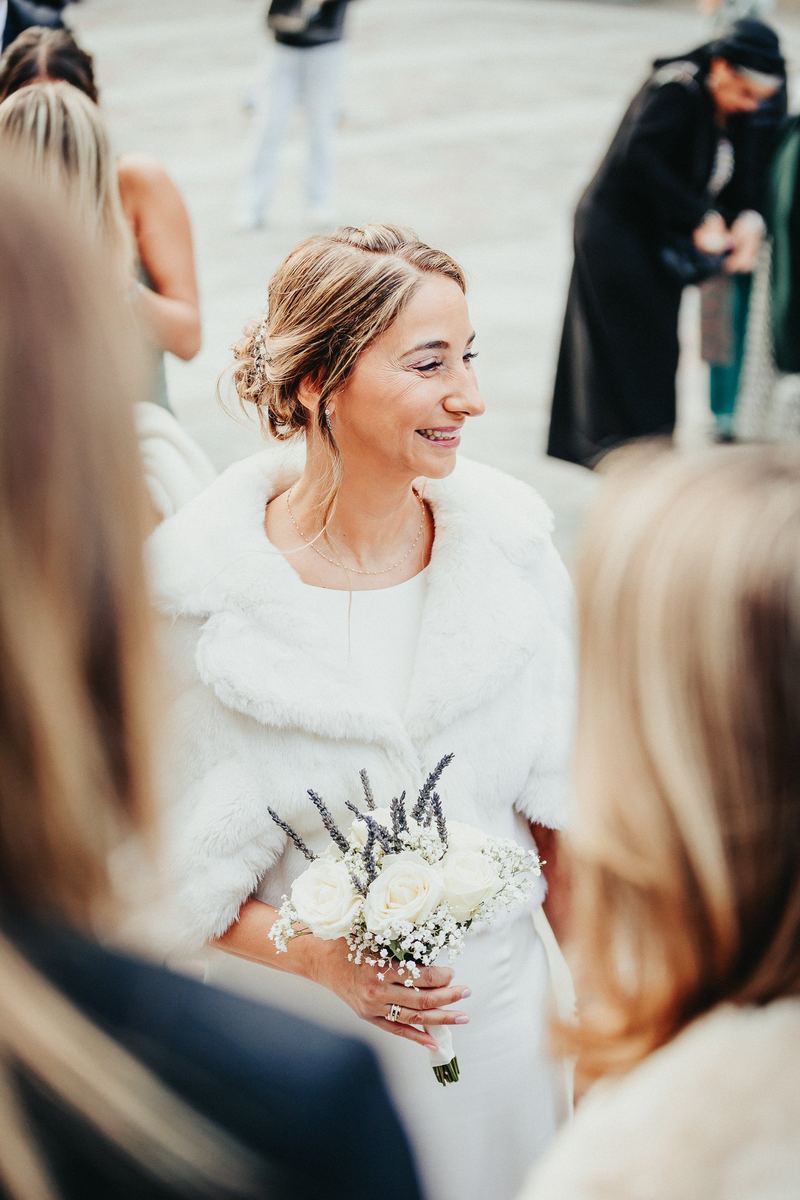 La mariée souriante au milieu des invités, étole blanche et bouquet à la main