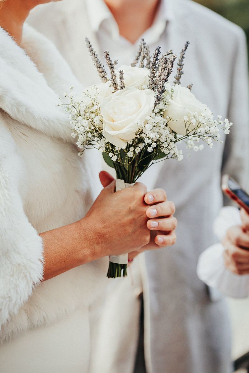 Bouquet de roses blanches et de lavande tenu par la mariée en étole de fourrure