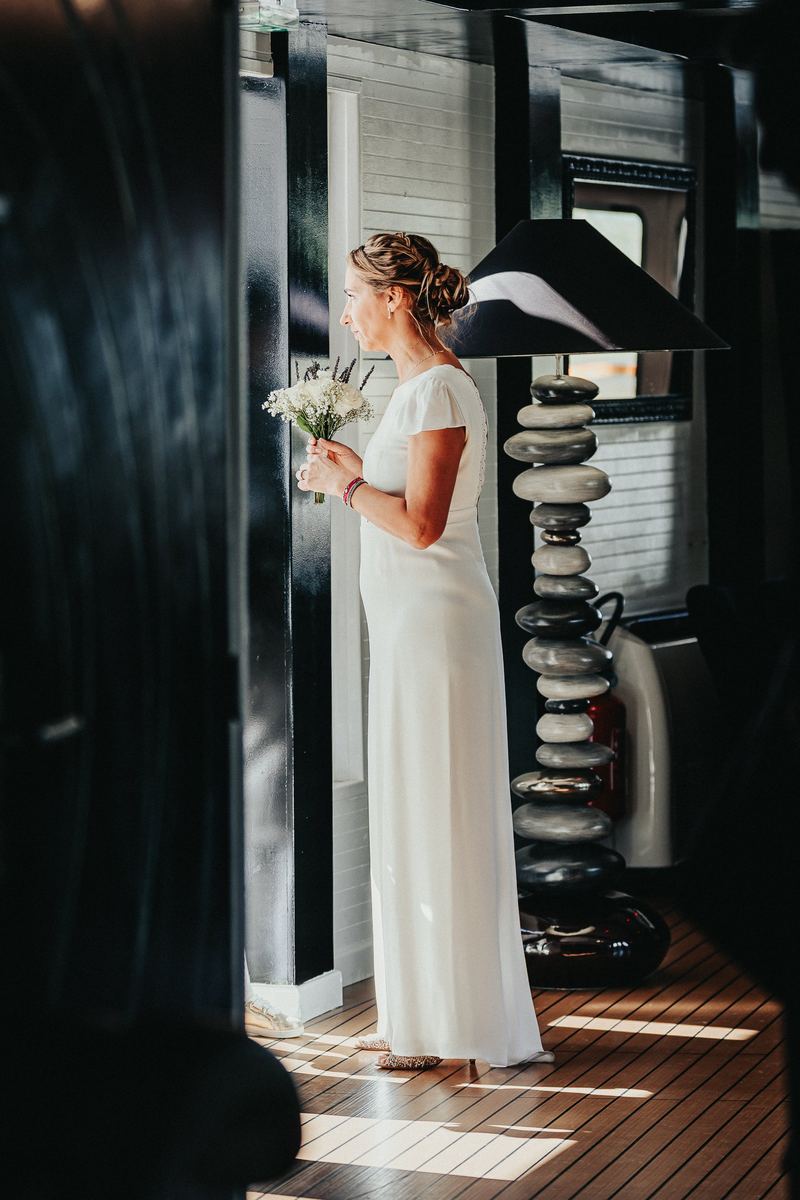 La mariée seule dans la coursive du bateau, bouquet à la main, avant la cérémonie