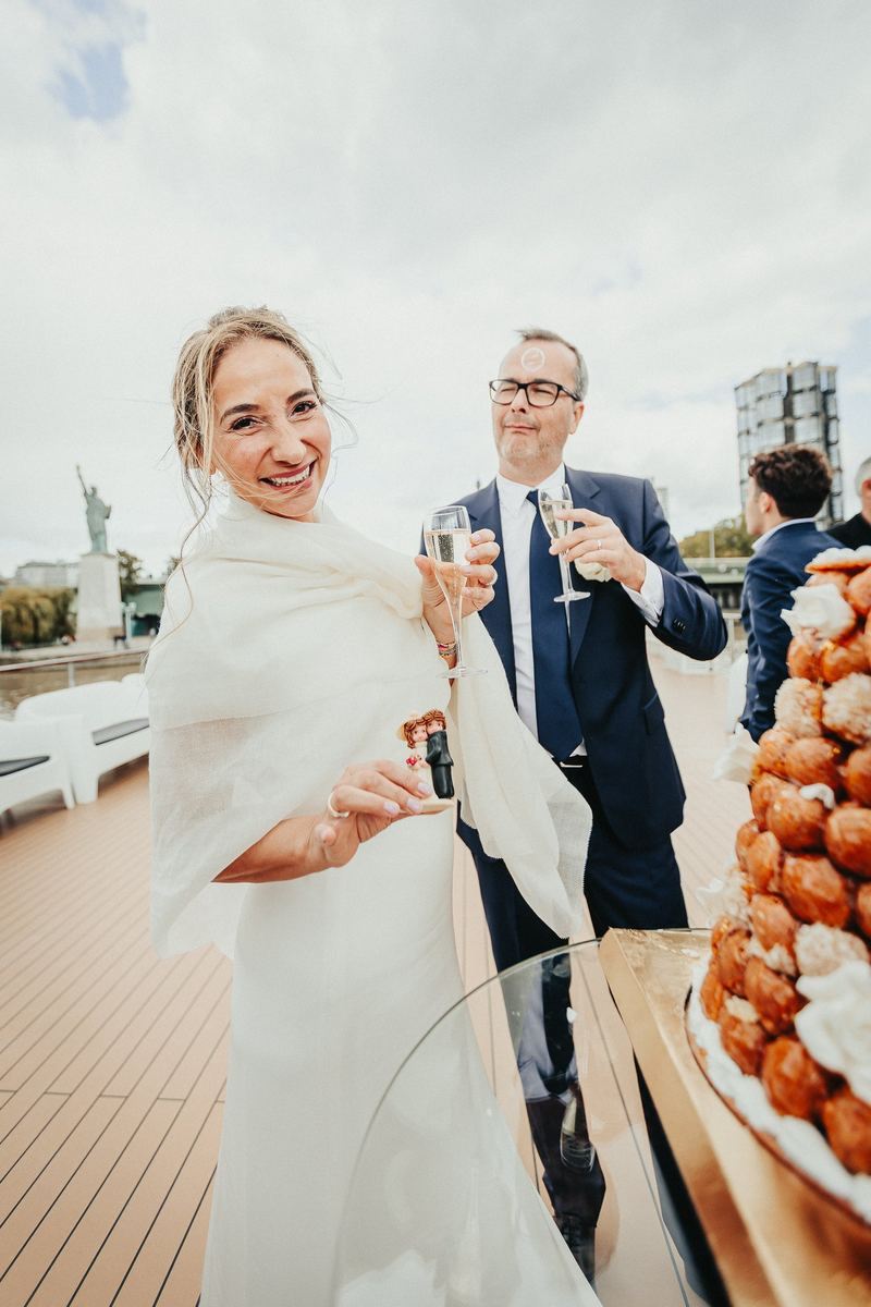 La mariée trinque au champagne sur le pont du bateau, réplique de la Statue de la Liberté derrière elle