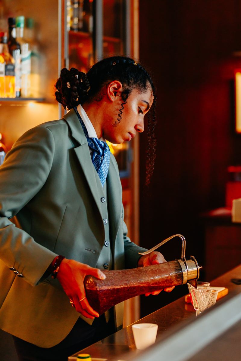 Barmaid verse une préparation derrière le comptoir, lumière ambrée