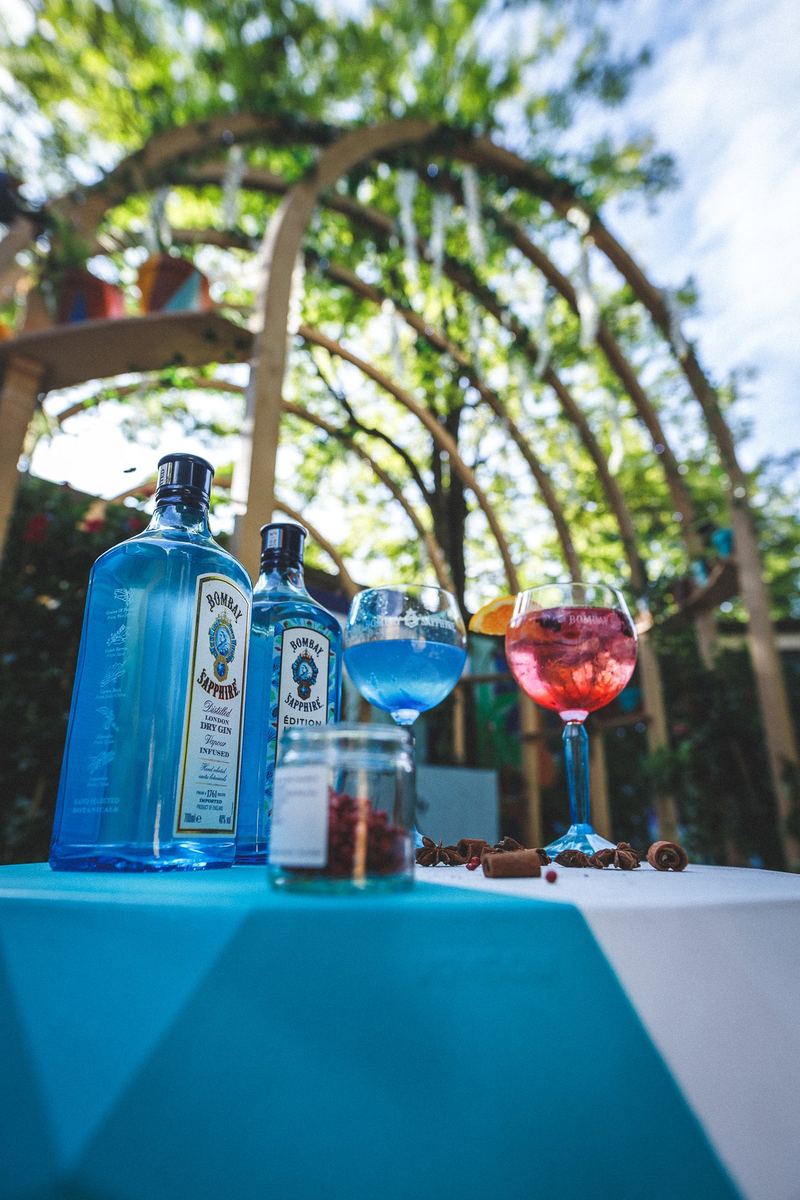 Bar extérieur : bouteilles de gin et cocktails colorés sous une pergola