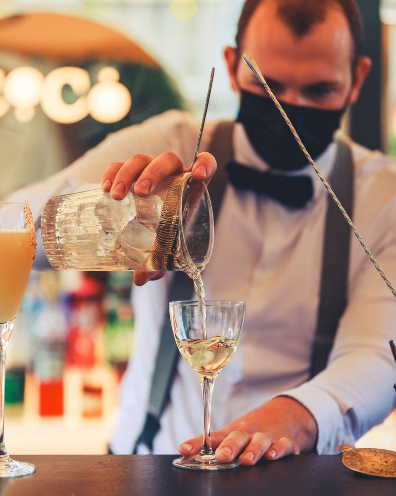 Barman masqué filtre un cocktail dans un verre à pied