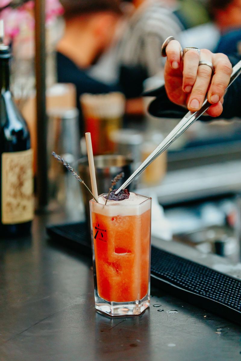 Barman termine un cocktail rouge à la pince, derrière le comptoir