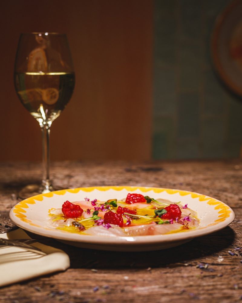 Carpaccio d’ananas et framboises, verre de vin blanc en arrière-plan