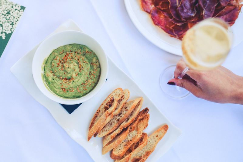 Une main trempe un morceau de pain dans un bol de houmous, devant une porte bleue