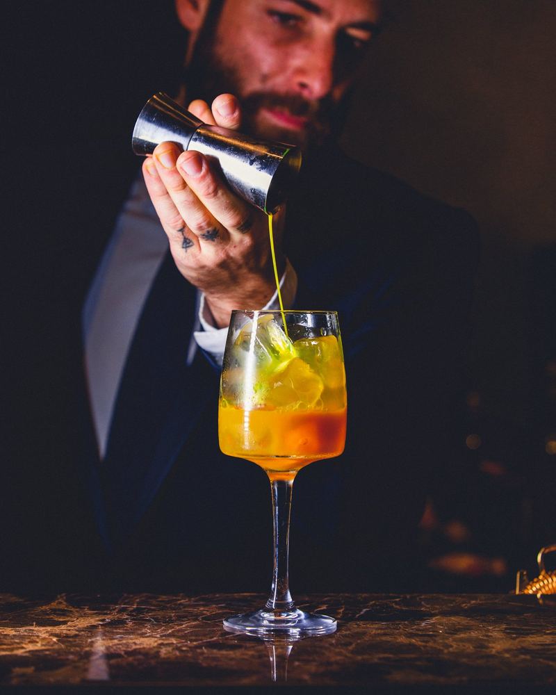 Barman verse un trait de sirop dans un spritz à l’orange