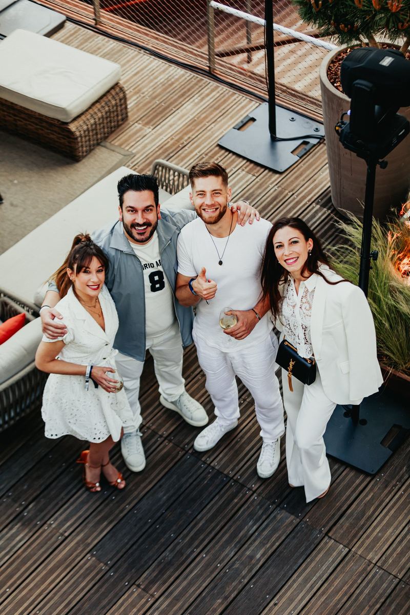 Quatre invités en tenue blanche posent sur la terrasse en bois, vus de haut