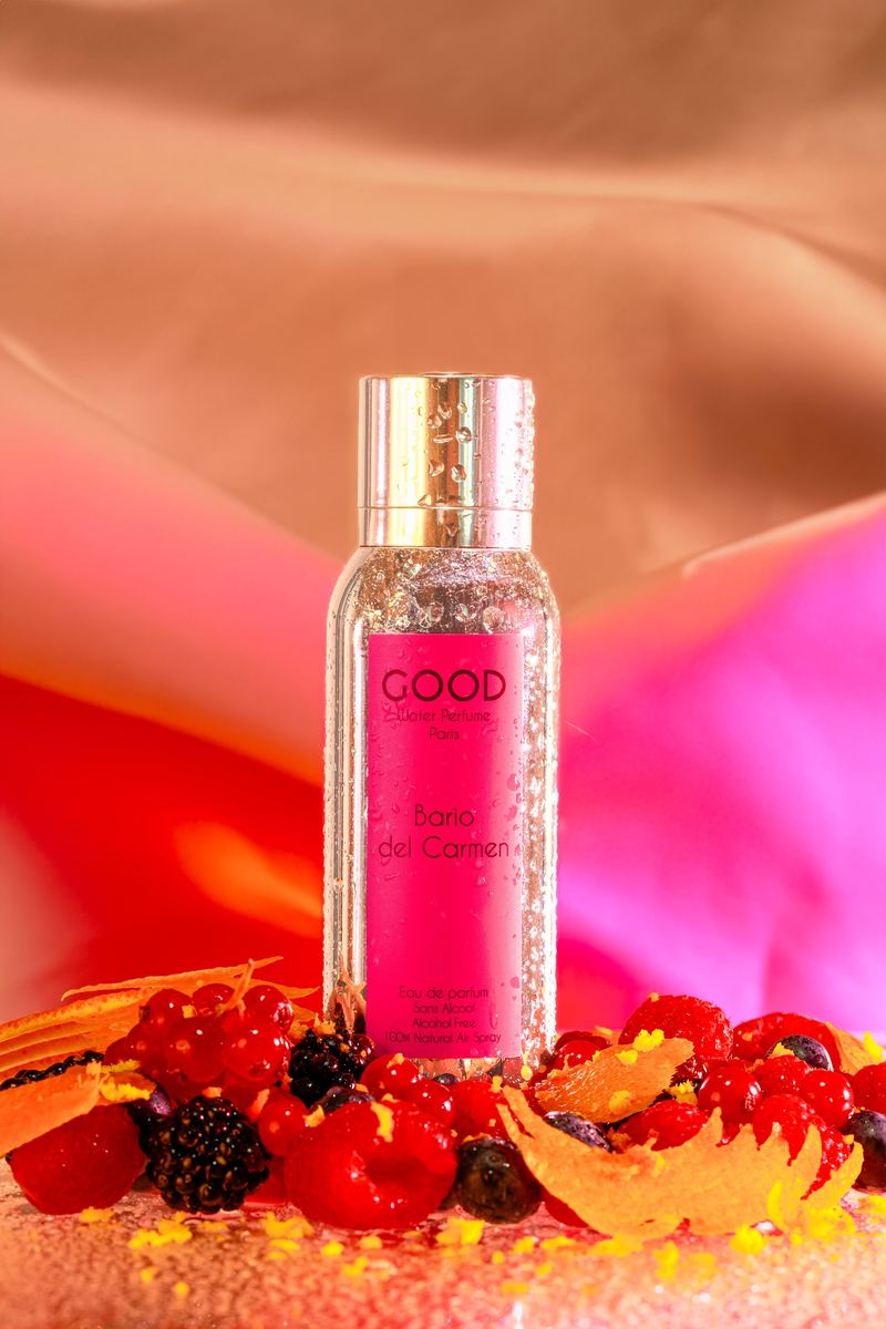 Packshot d’un parfum rose entouré de fruits rouges et de drapés