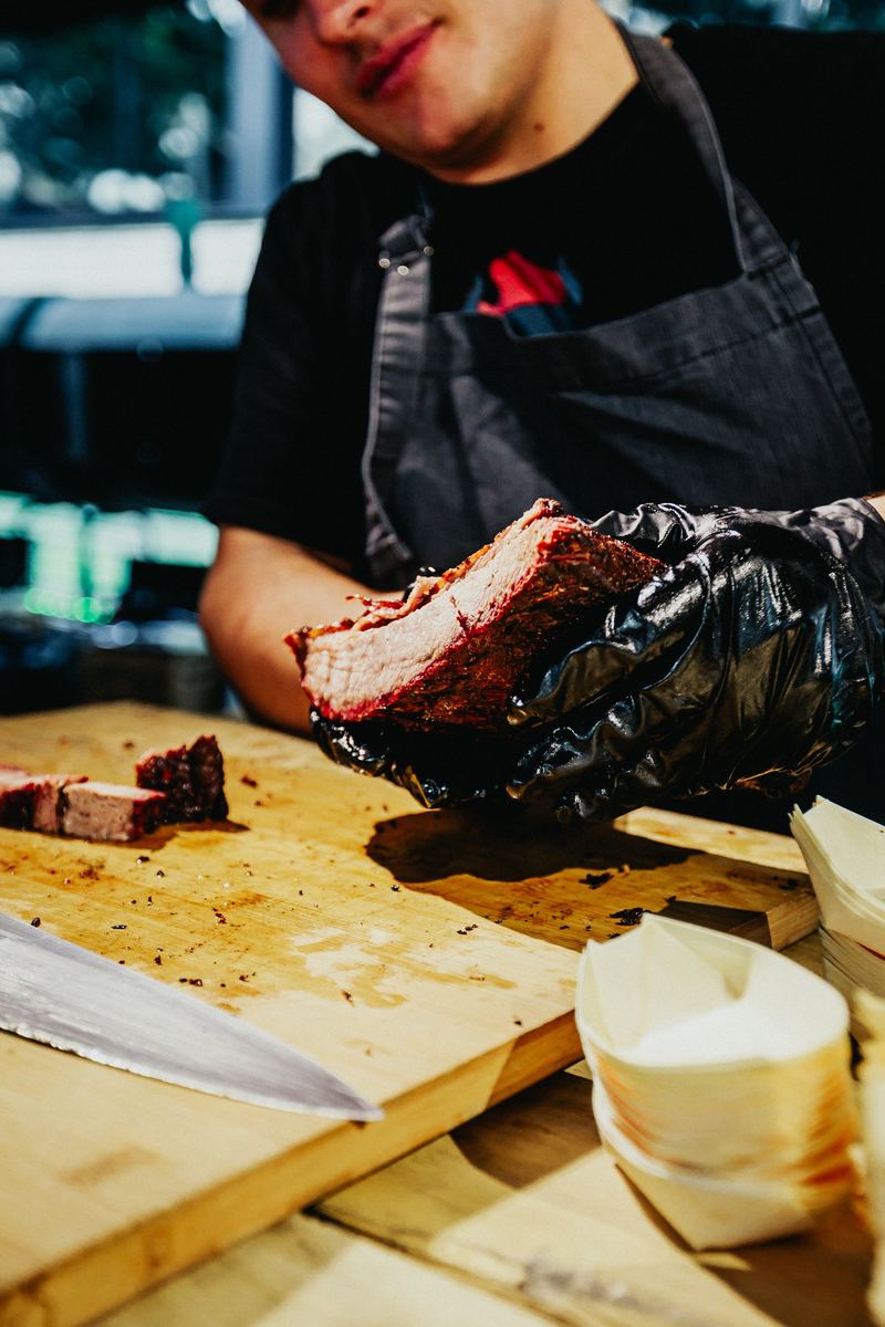 Le cuisinier tranche une pièce de viande fumée sur une planche