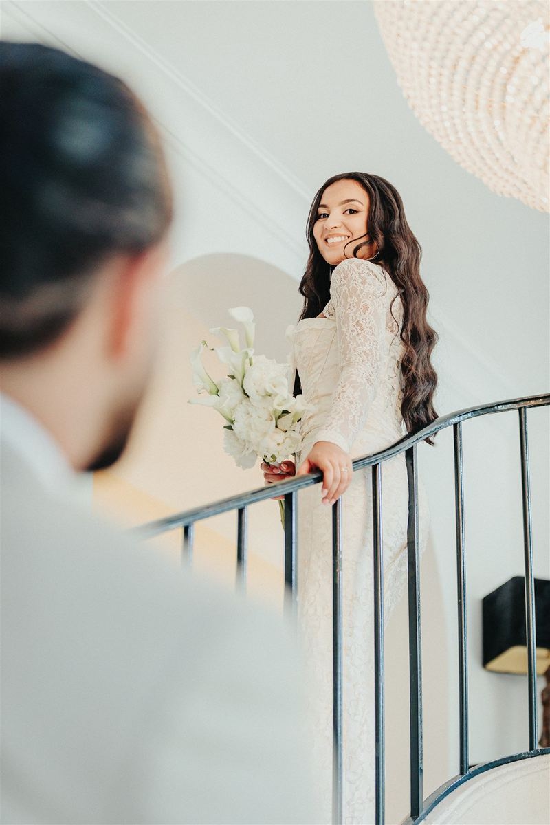 La mariée se retourne en souriant dans l’escalier, le marié de dos au premier plan